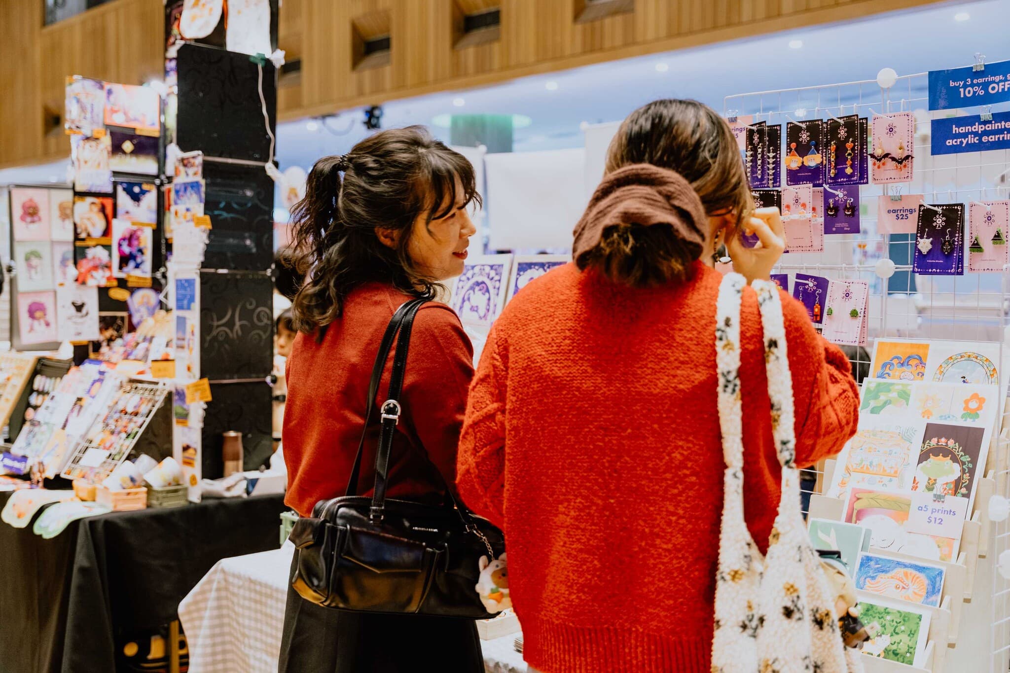 Shoppers browsing a wall of art prints and handmade earrings